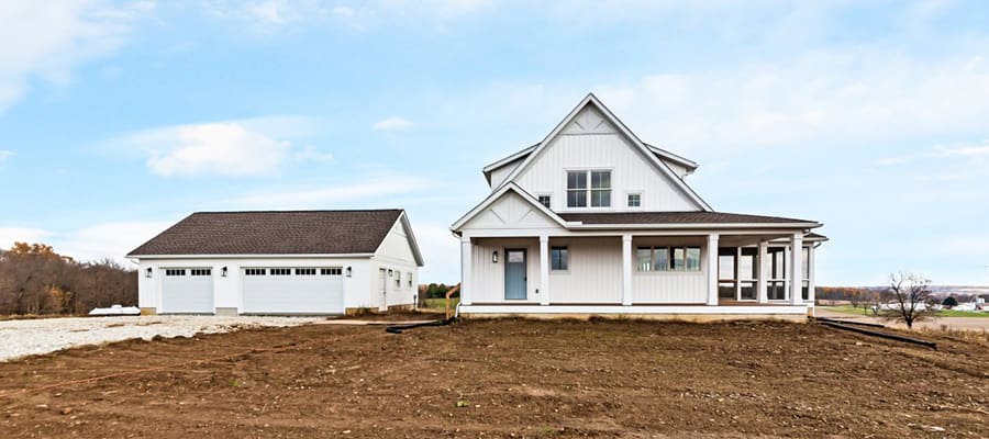 Fully custom home with detached garage and white board and batten siding.